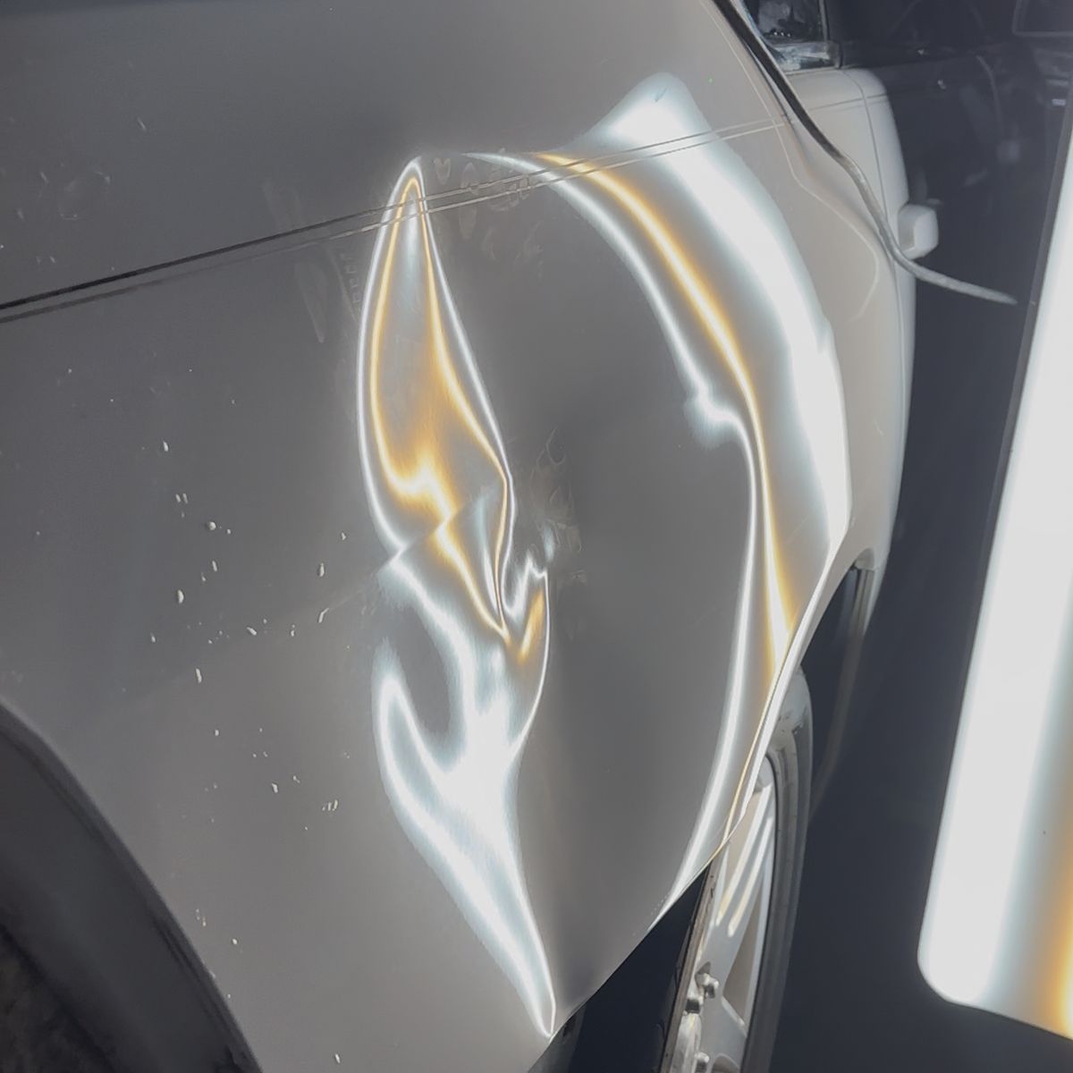 A dent on a car fender under a PDR reflection light, with the reflection lines bent around the damage